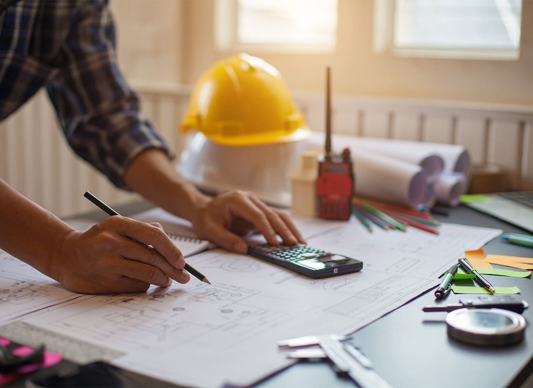 Insurance by Industry - Closeup View of a Contractor Looking Over Blueprints and Using a Calculator in his Office